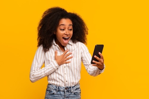 joyful-woman-amazed-by-smartphone-news-on-yellow-b-2024-04-09-18-20-49-utc